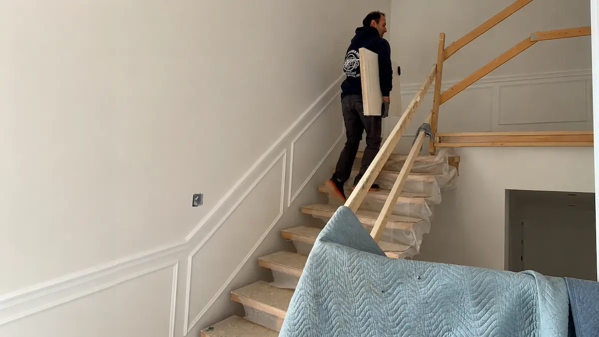 Professional movers carrying furniture safely up residential stairs